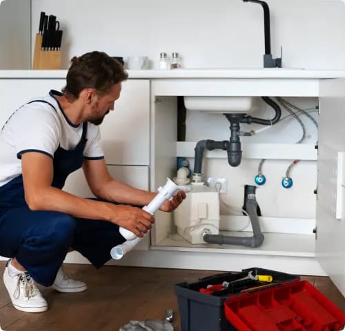 Plumber working under a kitchen sink with a red toolbox